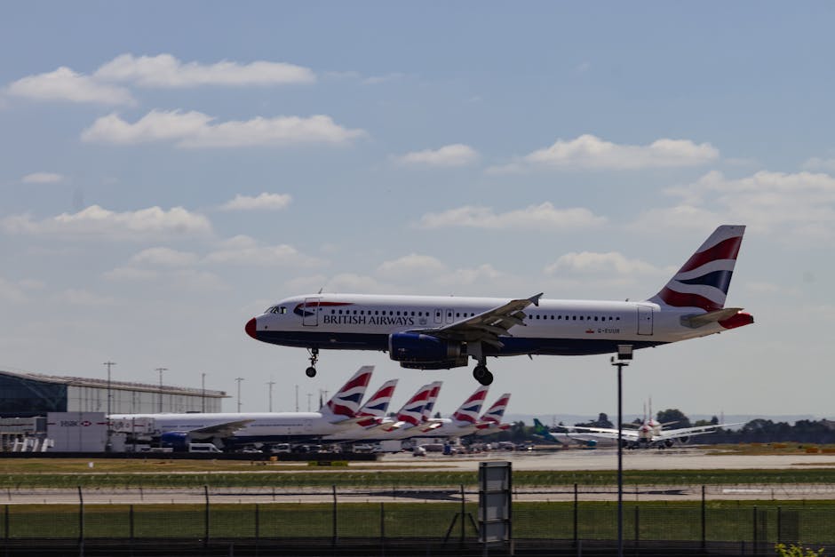 An aerial view of Heathrow Airport showing a large tarmac area with numerous parked commercial aircraft, primarily white with red and dark blue accents on their tails. The planes are arranged in rows,